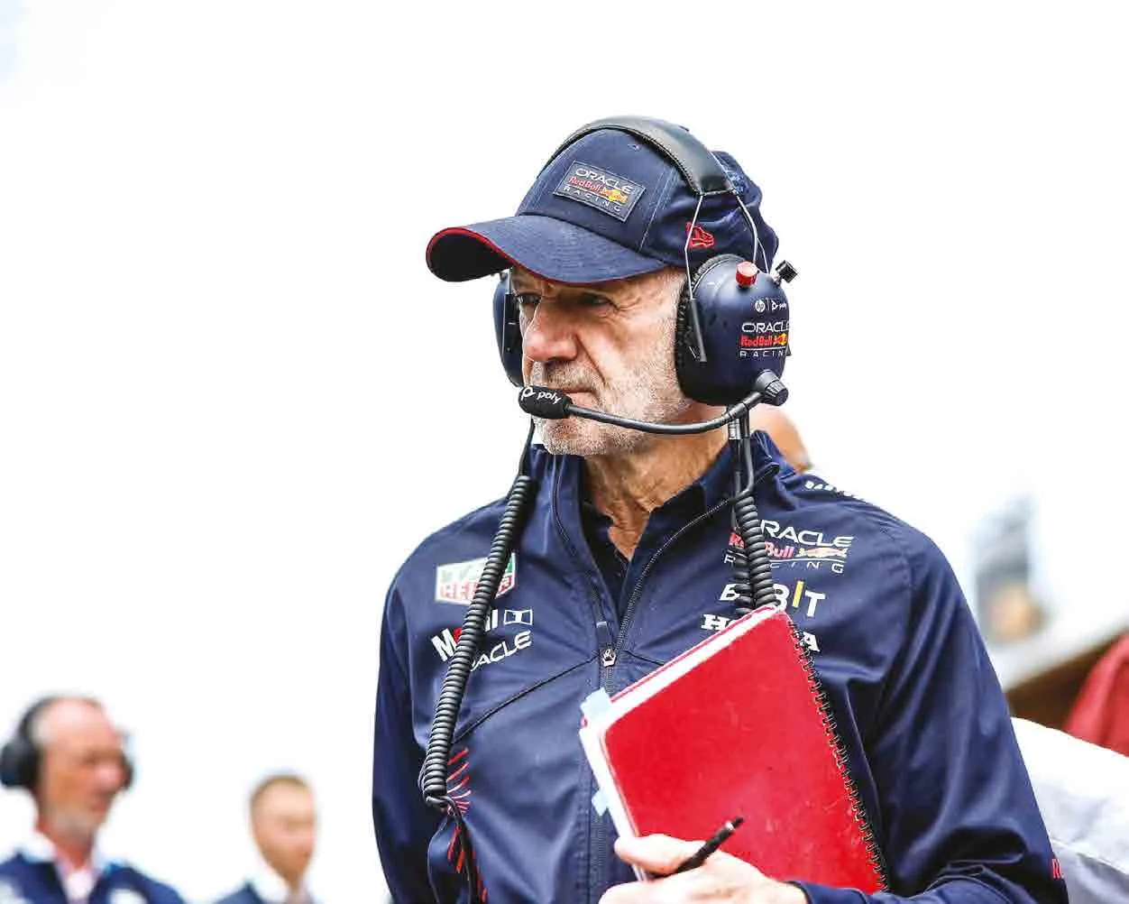 Adrian Newey con auriculares y una libreta roja en el pit lane
